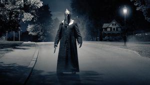 The Executioner, masked and all in black, carrying a large machete knife, looking menacing on a dark street in a small home town