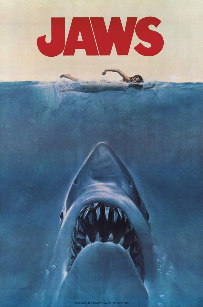 The Jaws 1975 poster. A woman is swimming in the ocean, and we can see the shark swimming up towards her from the depths.